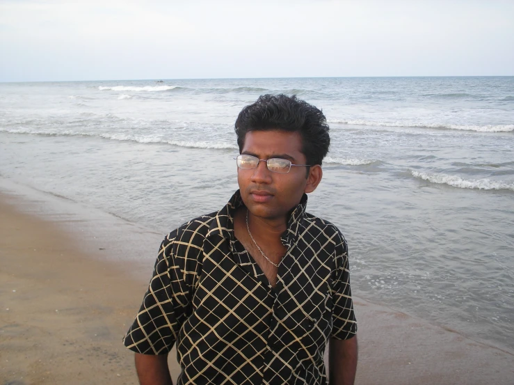young man wearing glasses standing on beach next to ocean