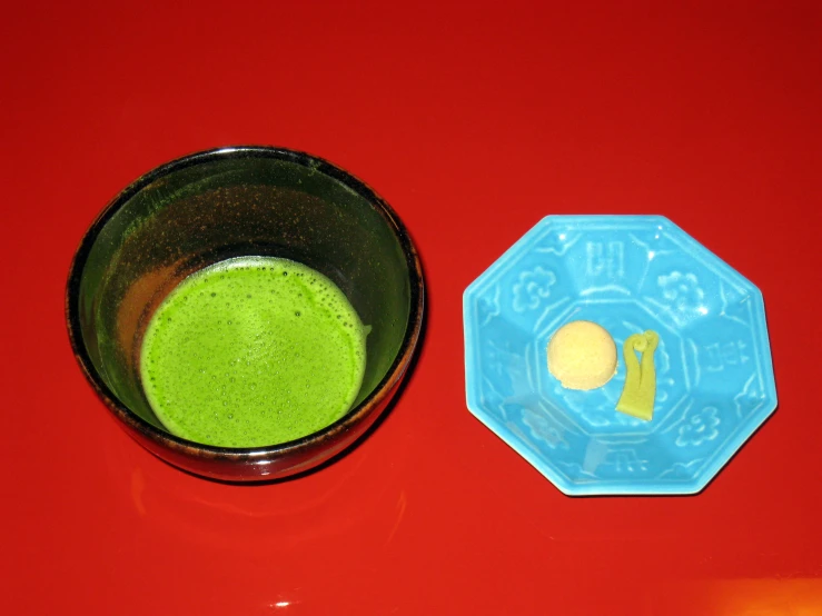 a cup filled with green liquid and a blue bowl with a banana on it
