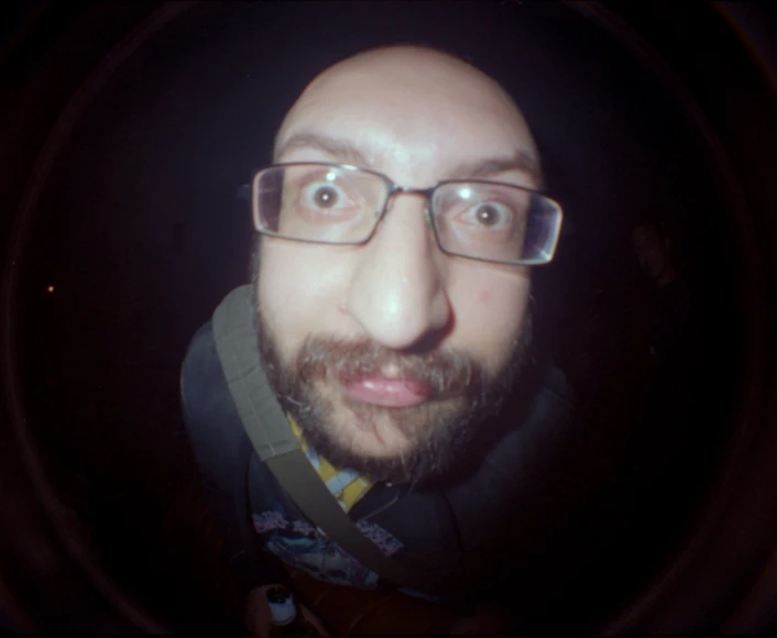 a man with glasses on standing in front of a camera