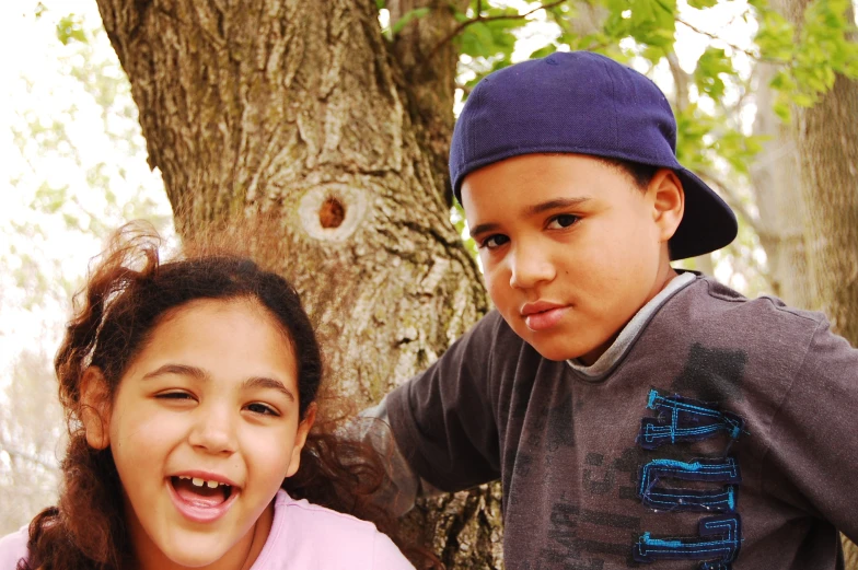 two children stand next to each other near a tree