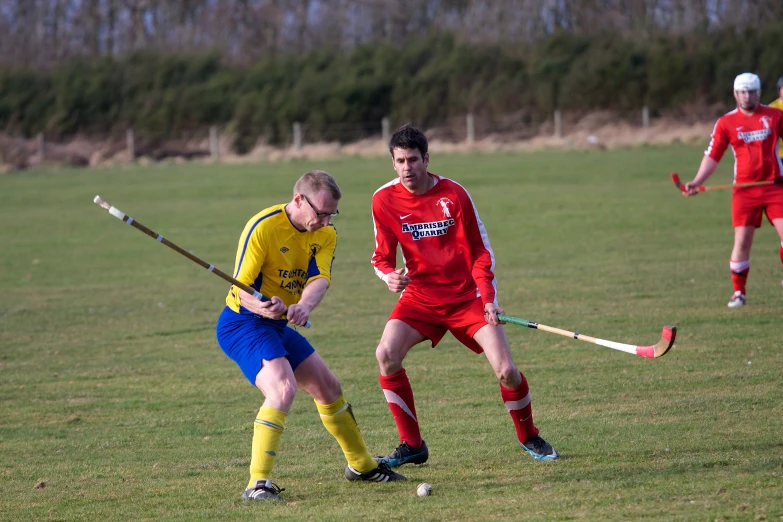 two people running towards each other in a field with a soccer ball and stick