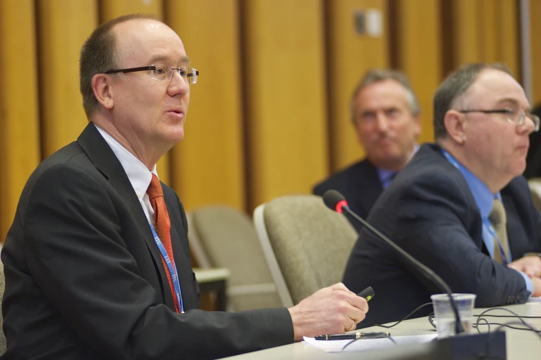 several men are sitting at a conference table in front of microphones