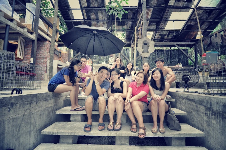 people sitting on concrete stairs under a black umbrella