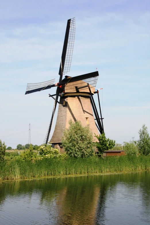 a windmill sitting next to the water in the grass