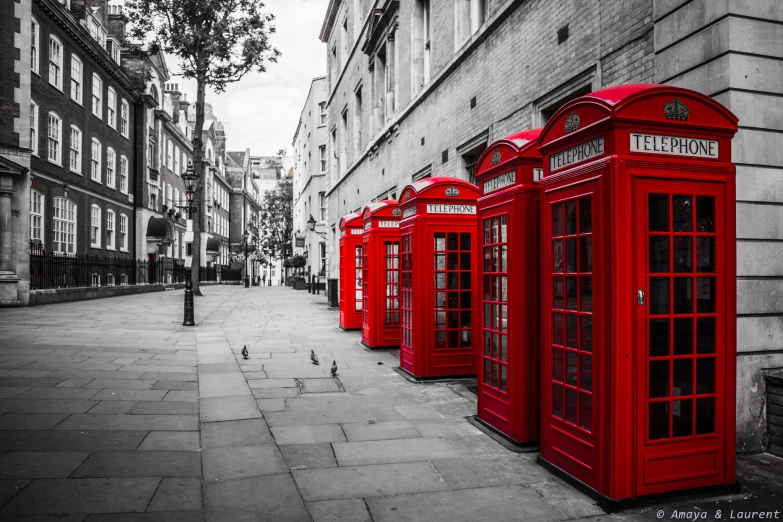 four red phone booths sitting on the side of a street