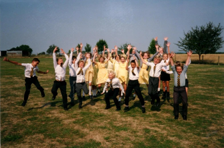 a group of schoolgirl's and boys are standing in the grass posing for a picture