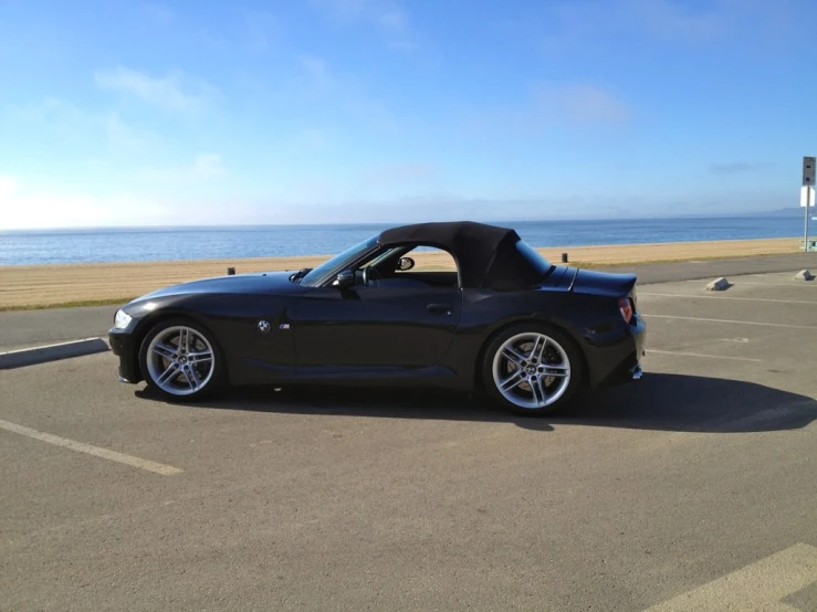 black sports car parked in empty parking lot with ocean in background
