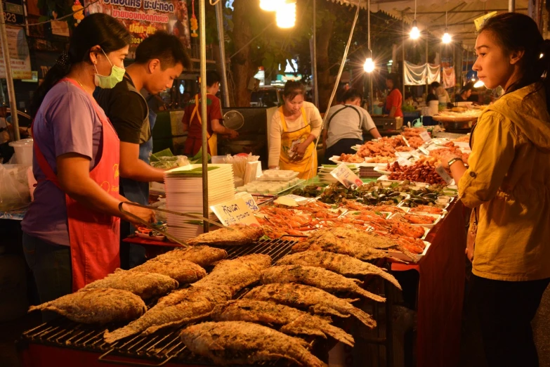 several people are at a food stand with various types of foods on a grill