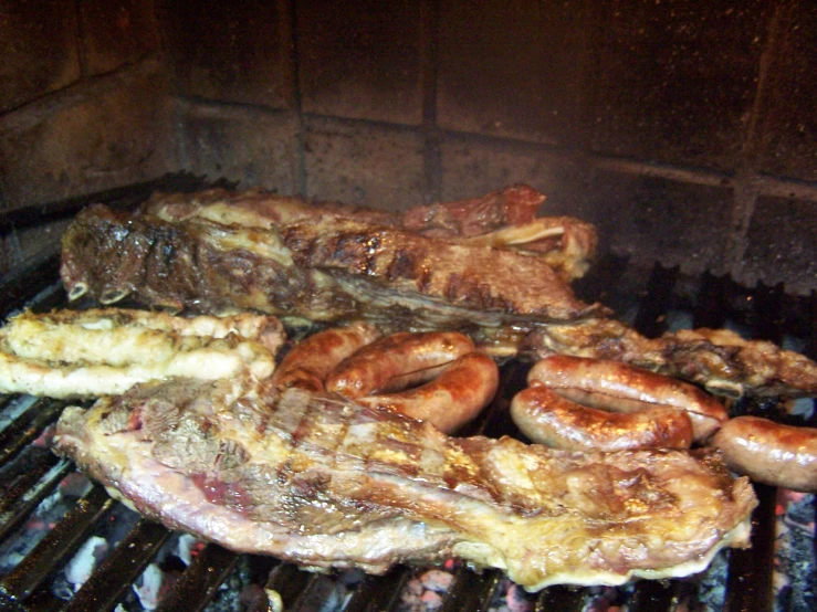 a grill full of sausage, meat, and onions cooking on it