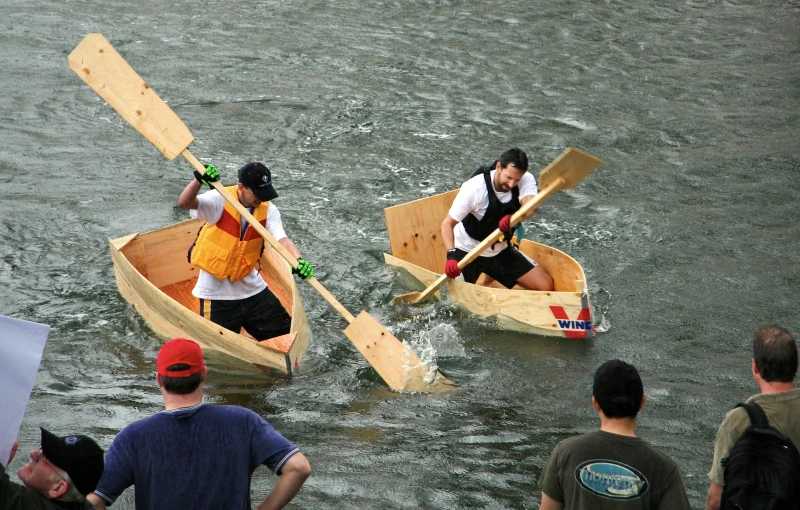 two people wearing life vests paddle small wooden boats