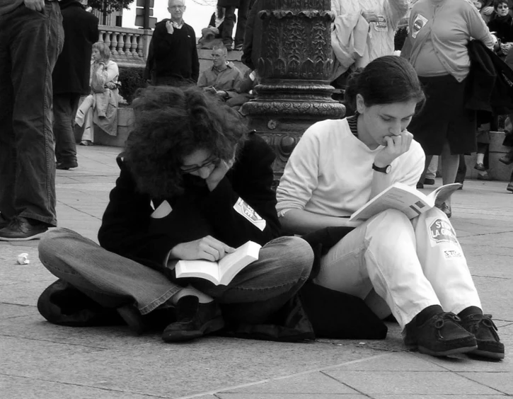 two people sitting on the ground reading books