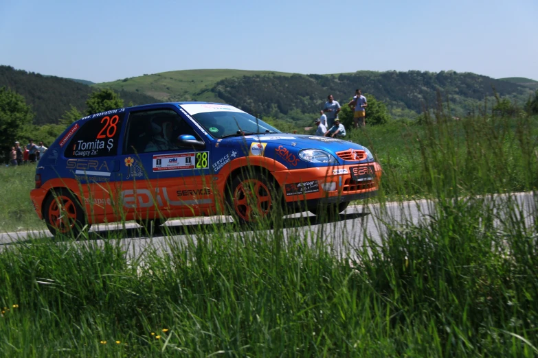 a bright orange and blue car with numbers is driving on a road