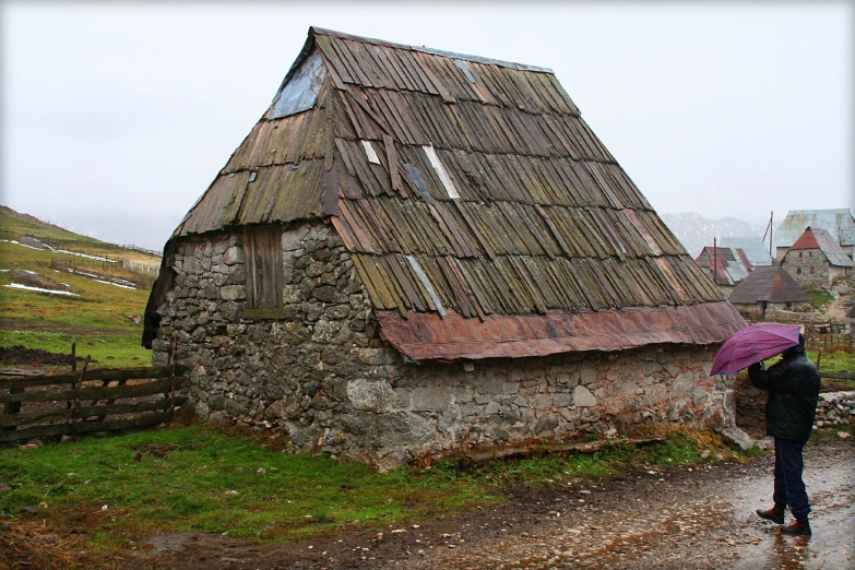 a person holds an umbrella in the rain next to an old brick barn