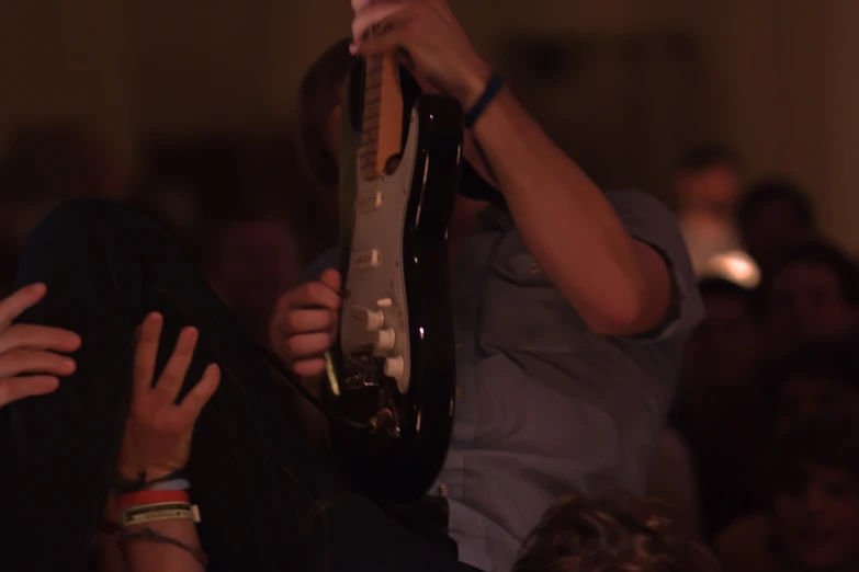 man holding up neck guitar strings while sitting in audience