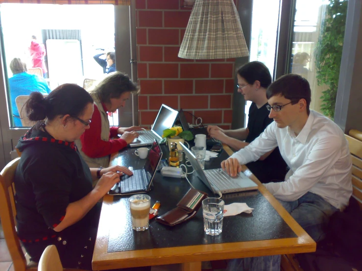 four people sitting around a table using laptop computers