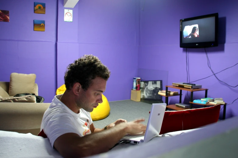 a man is working on his laptop in a purple bedroom