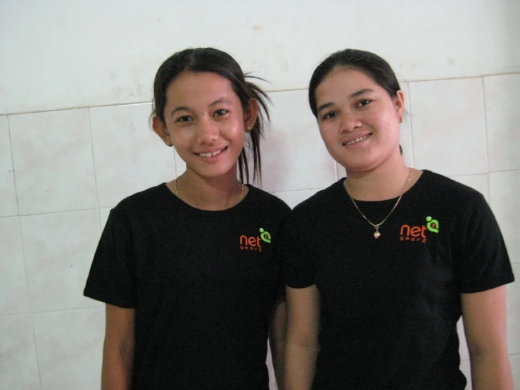 two asian women in black shirts are standing near a wall