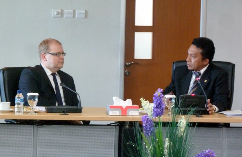 two men in suits sitting at desks in an office