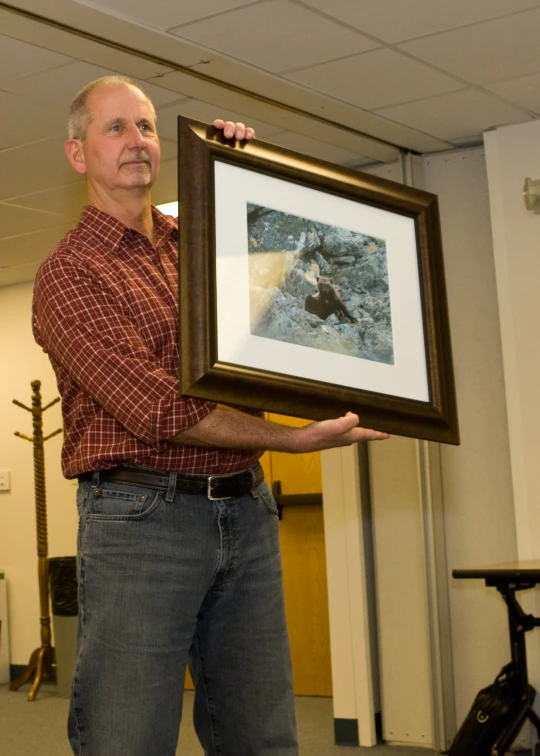 a man in jeans holds a framed painting