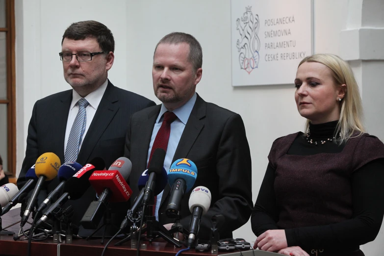 people in suits and ties stand behind microphones in front of several reporters