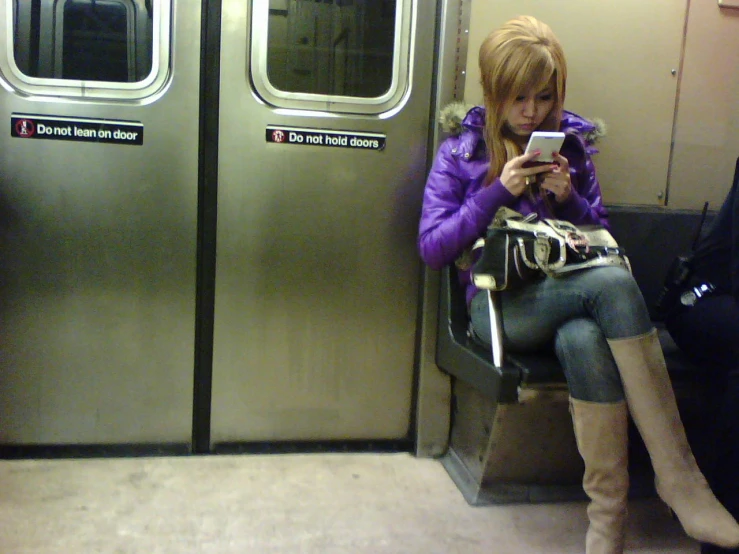 a woman in purple jacket sitting on a subway bench and looking at her cell phone