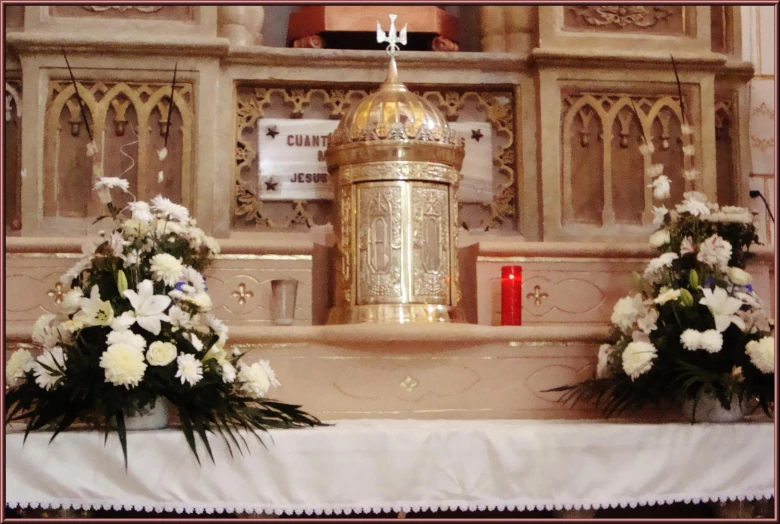 a priest sitting in front of a gold alter with flowers