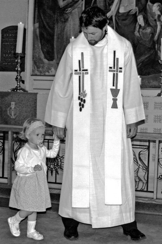 a child stands next to a priest in front of a church window