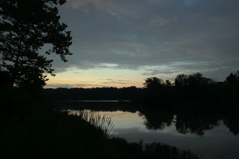 a dark lake surrounded by trees and a cloudy sky