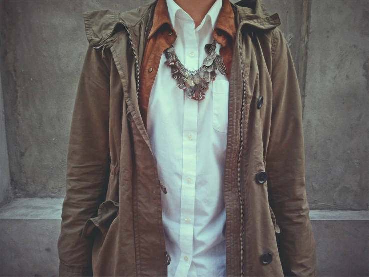 a man in an brown jacket wearing a white shirt and a necklace
