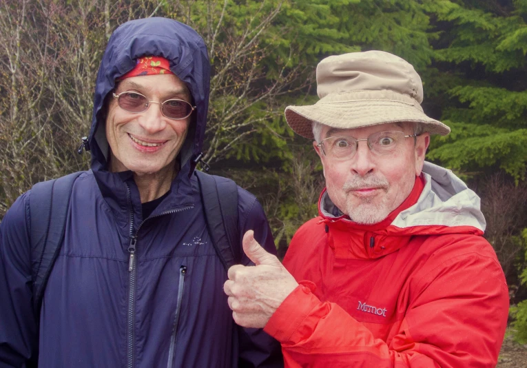 a man with a hat gives a thumbs up as a woman stands behind him