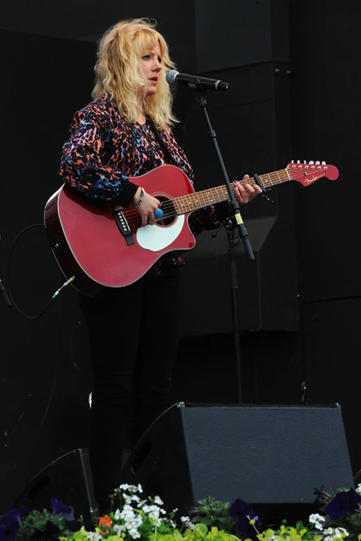 the woman is singing and playing her red guitar