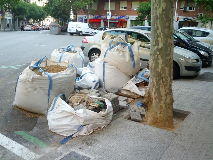 bags of dirt on the sidewalk next to a car and trees
