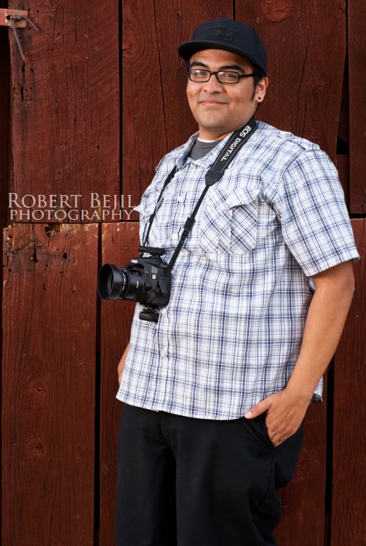 a man poses in front of a wooden fence