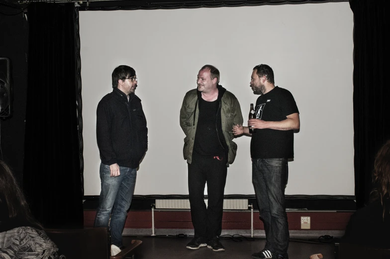 three men are standing around in front of a large white screen