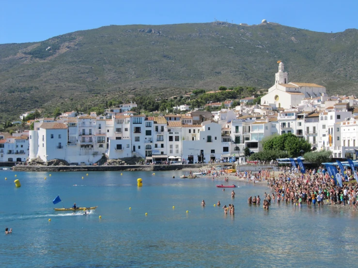 people are gathered around and on the water with a hill in the background