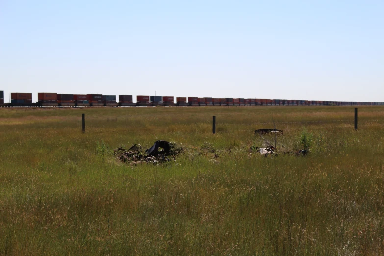 a field has some dirt and grass with a freight container in the distance
