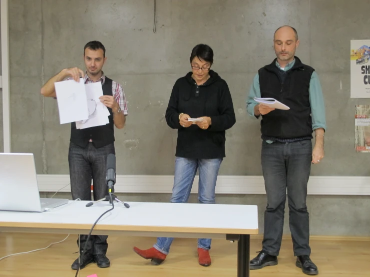 three people standing in front of a laptop on a table