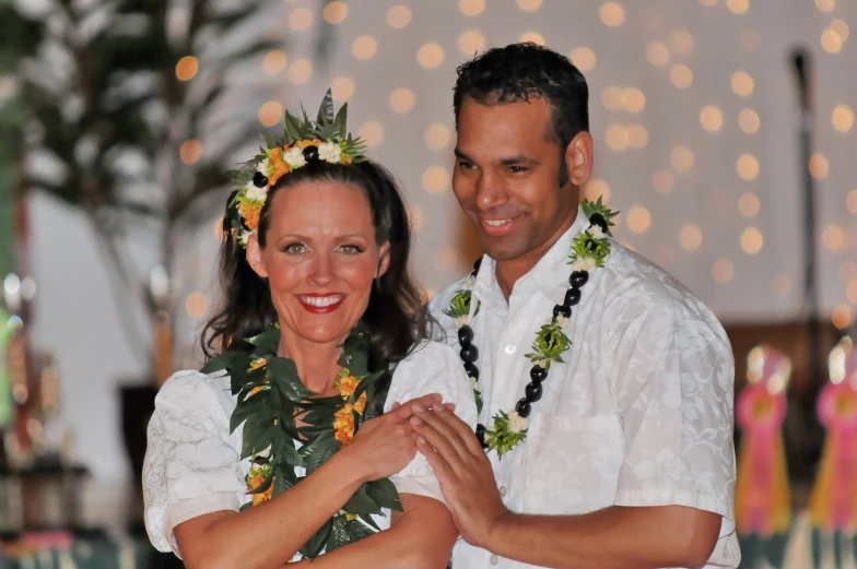 a man and woman wearing leis smile as they hold each other