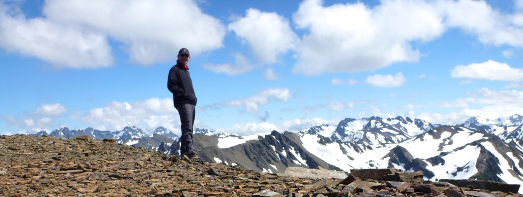 a person stands on top of a mountain with a view of snowy mountains