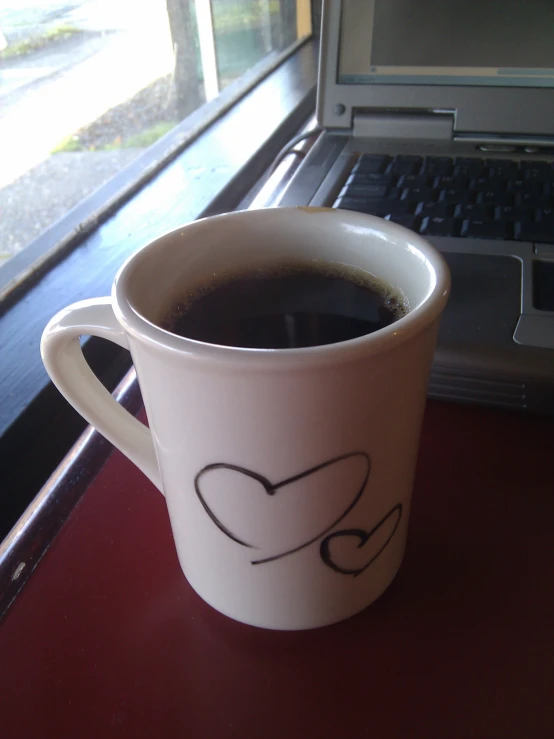 a coffee cup is sitting on the table near a laptop