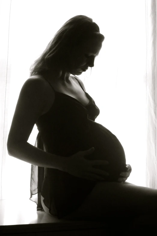 pregnant woman posing by a window in the light