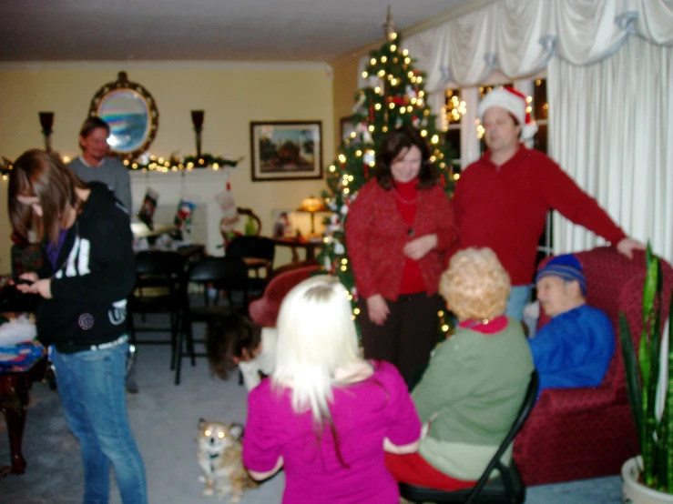 a group of people are sitting and standing around a christmas tree