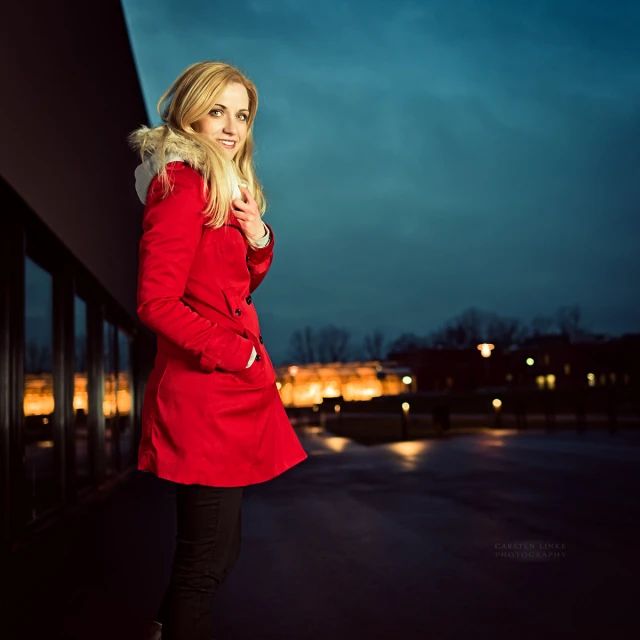woman in red jacket standing against wall and looking down