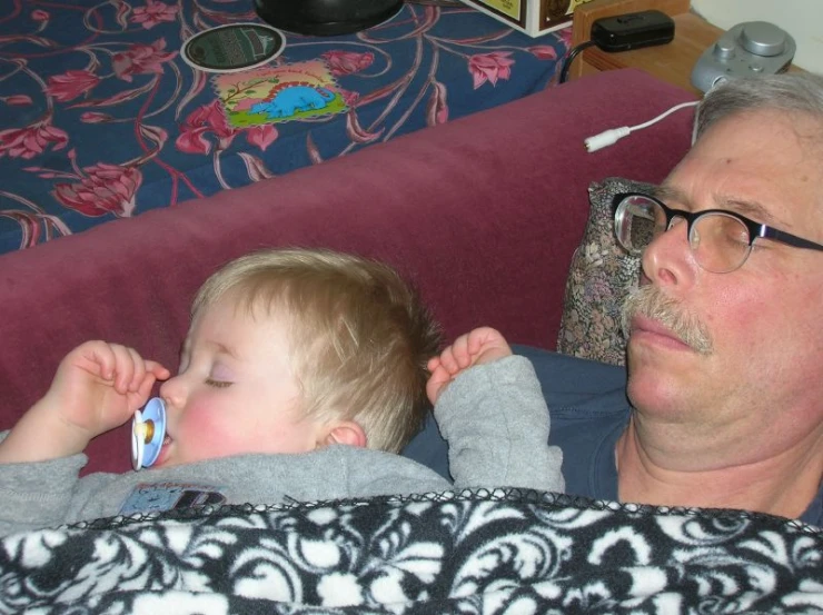 an adult holds a baby and the child has a toothbrush in his ear