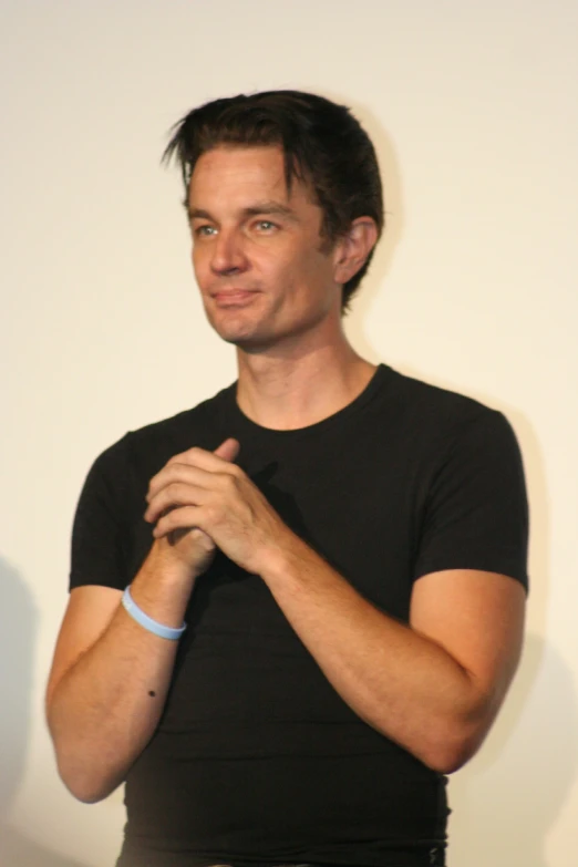 a young man with his hands together in front of a white wall