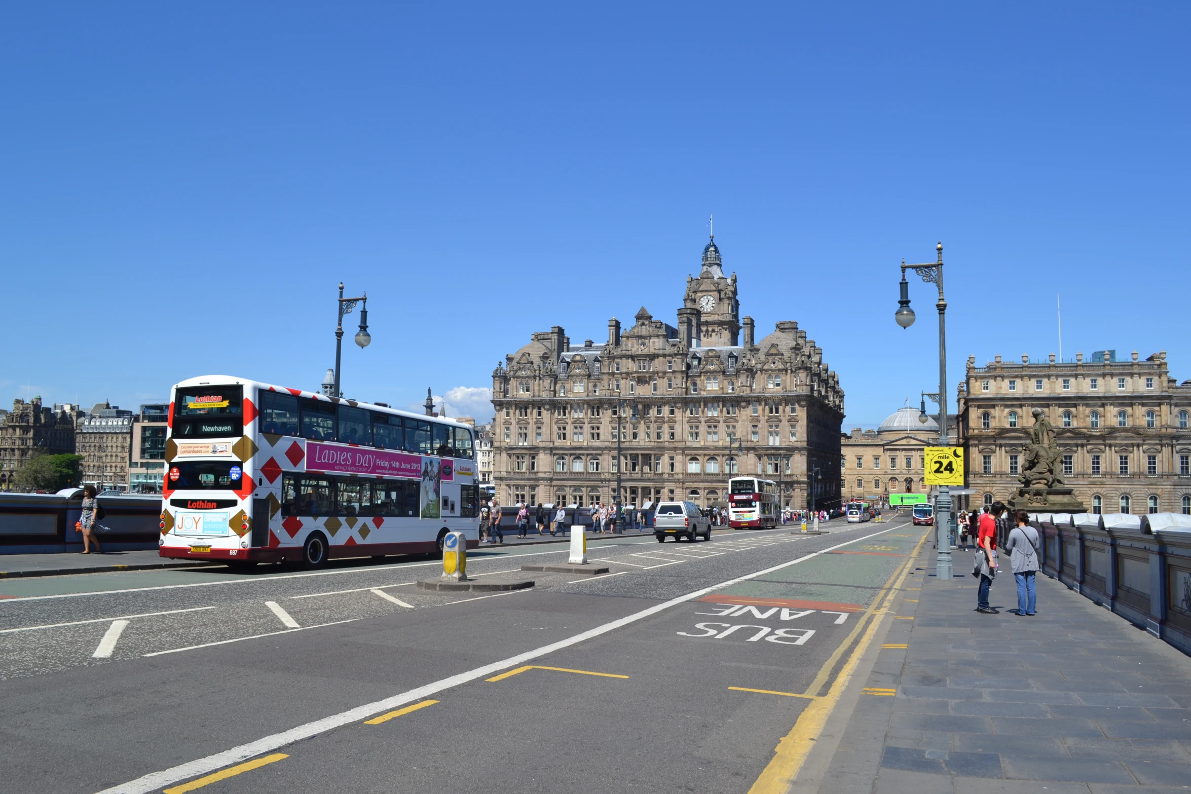 double decker buses and pedestrians on the street in front of a castle