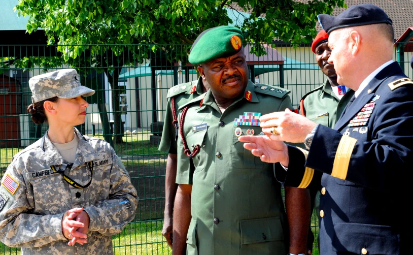 two military men, one in a green hat and one in a gray suit, are being interviewed by a woman in uniform