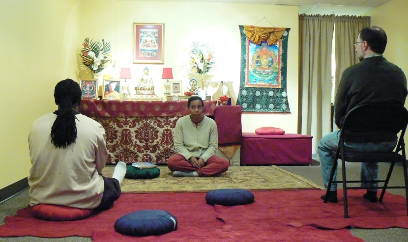 four people sit in a living room on the floor, with bright colored fabrics