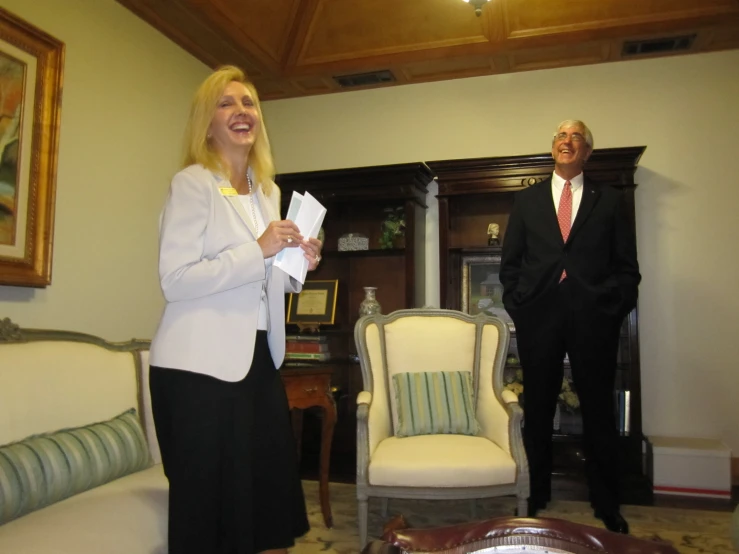 a man in a business suit and woman in a white top smile in a living room