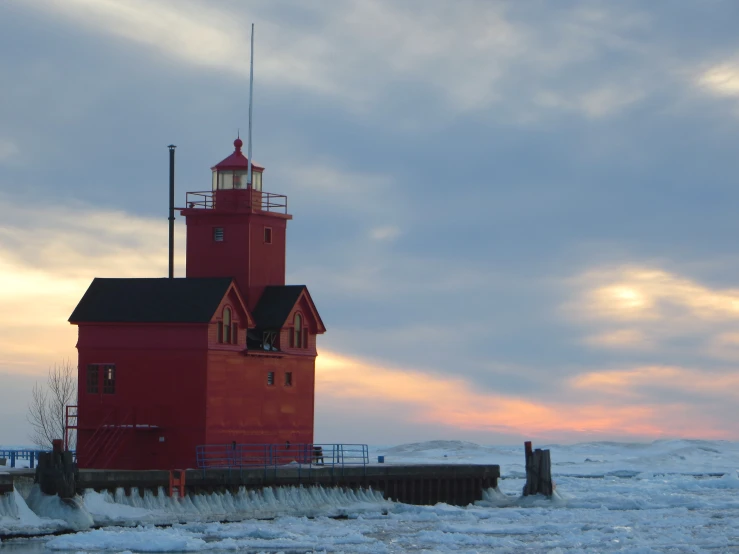 the lighthouse stands out in the snow as the sun is setting